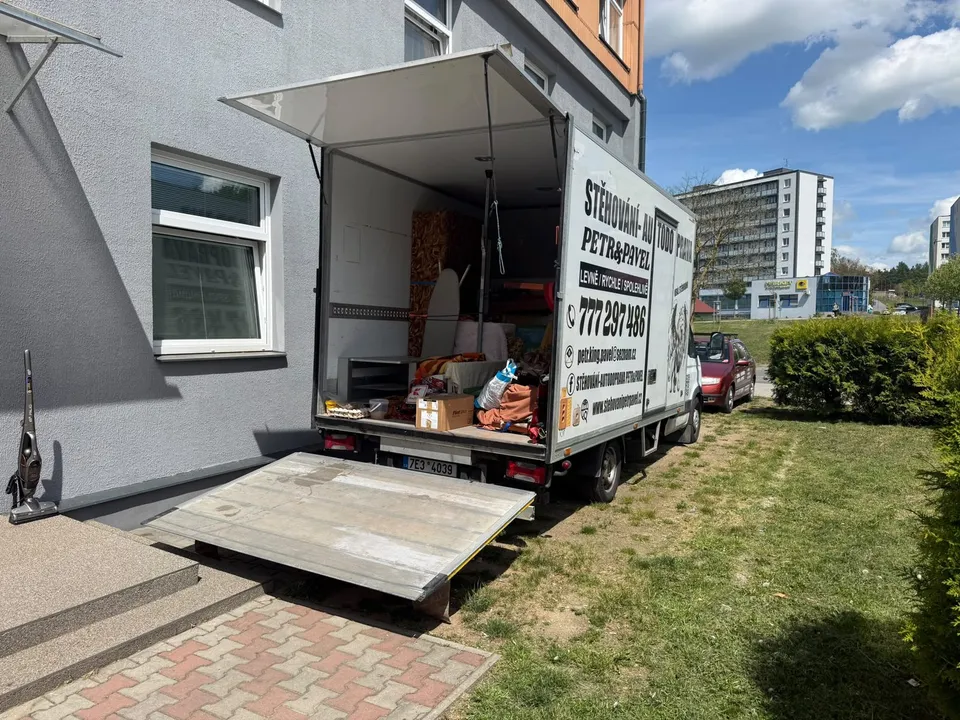 Stěhovací vůz Petr & Pavel se spuštěným hydraulickým čelem u bytového domu